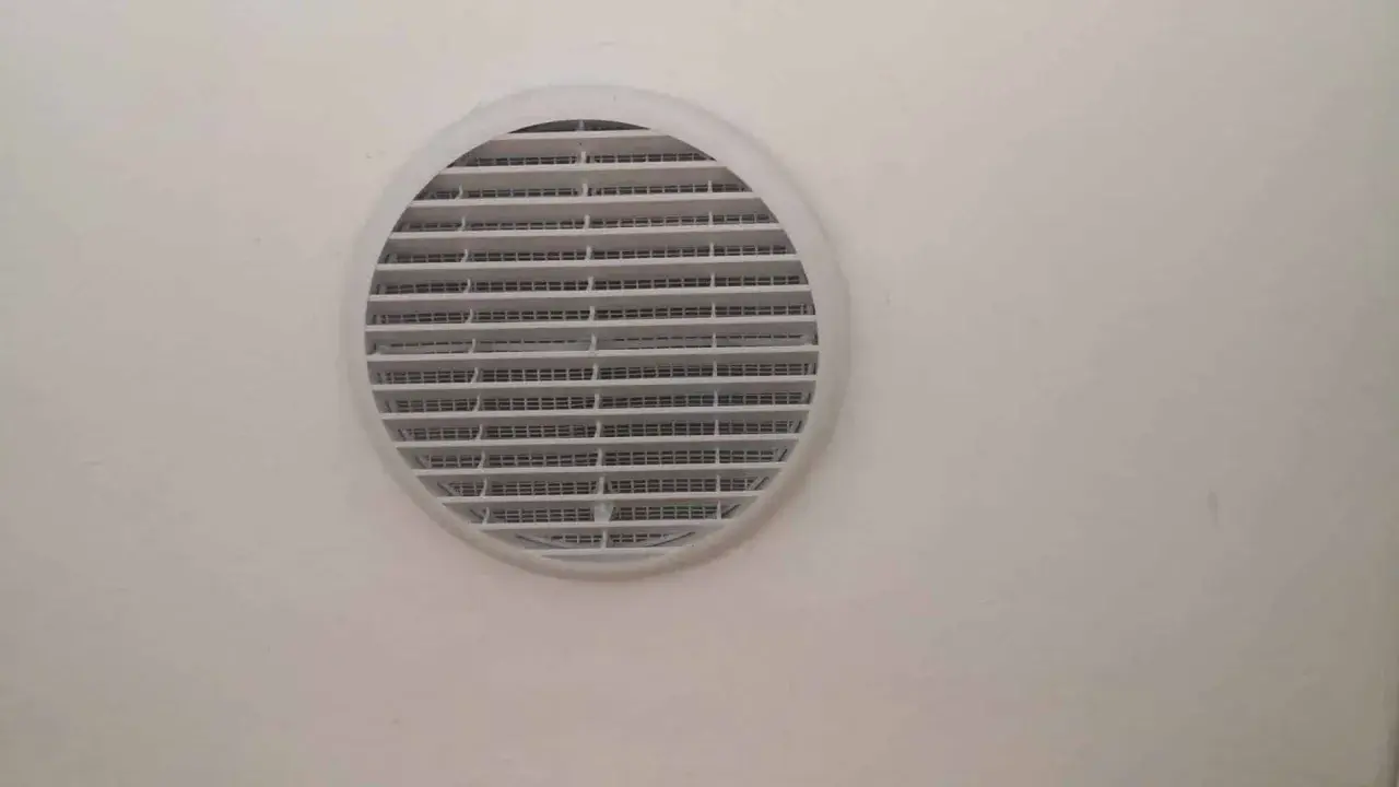 Foro ventilazione cucina entra freddo. La griglia bianca circolare è montata su una parete chiara.