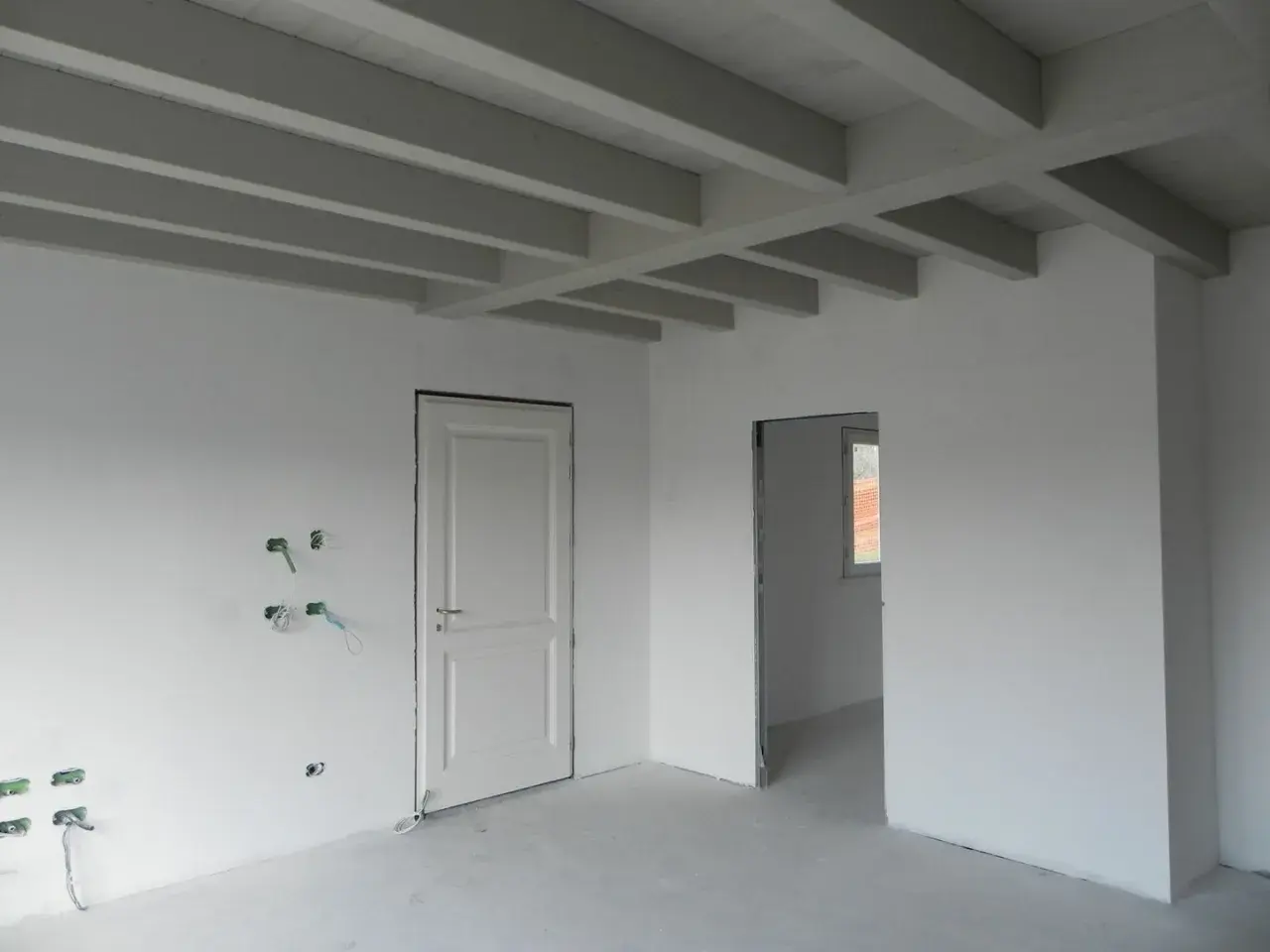 Interno in fase di finitura: pareti bianche, travi a vista e predisposizioni elettriche. Lo spessore intonaco interno è uniforme.