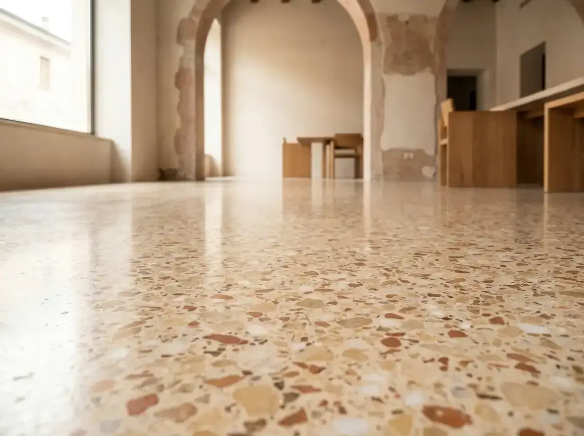 Pavimento lucido in cocciopesto veneziano, con riflessi di luce e mobili in legno sullo sfondo.