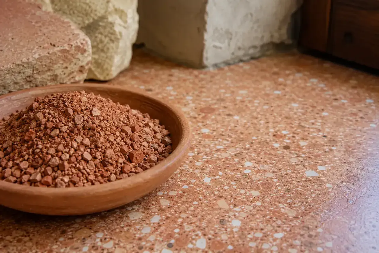 Ciotola di terra rossa, materiale grezzo per il rinzaffo significato. Sotto blocchi di pietra e un pavimento in graniglia.