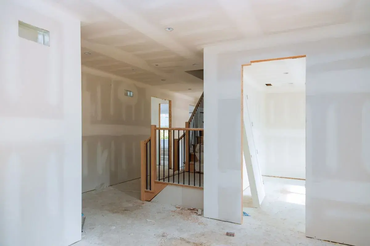Interno in costruzione, con pareti in cartongesso grezzo e una scala. Ideale per chi cerca come realizzare una parete divisoria economica.
