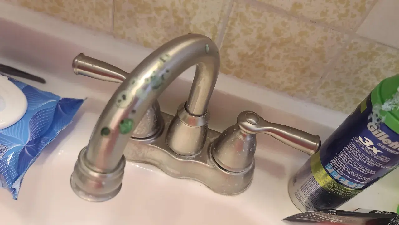 Rubinetti del bagno con calcare verde incrostato. Accanto, salviettine e una bomboletta di schiuma da barba.