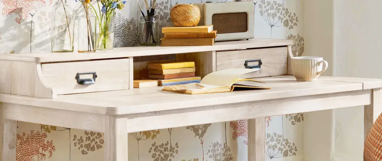 Scrivania chiara con cassetti, libri, tazza e radio vintage. Ideale per chi vuole imparare come verniciare un mobile da marrone a bianco.