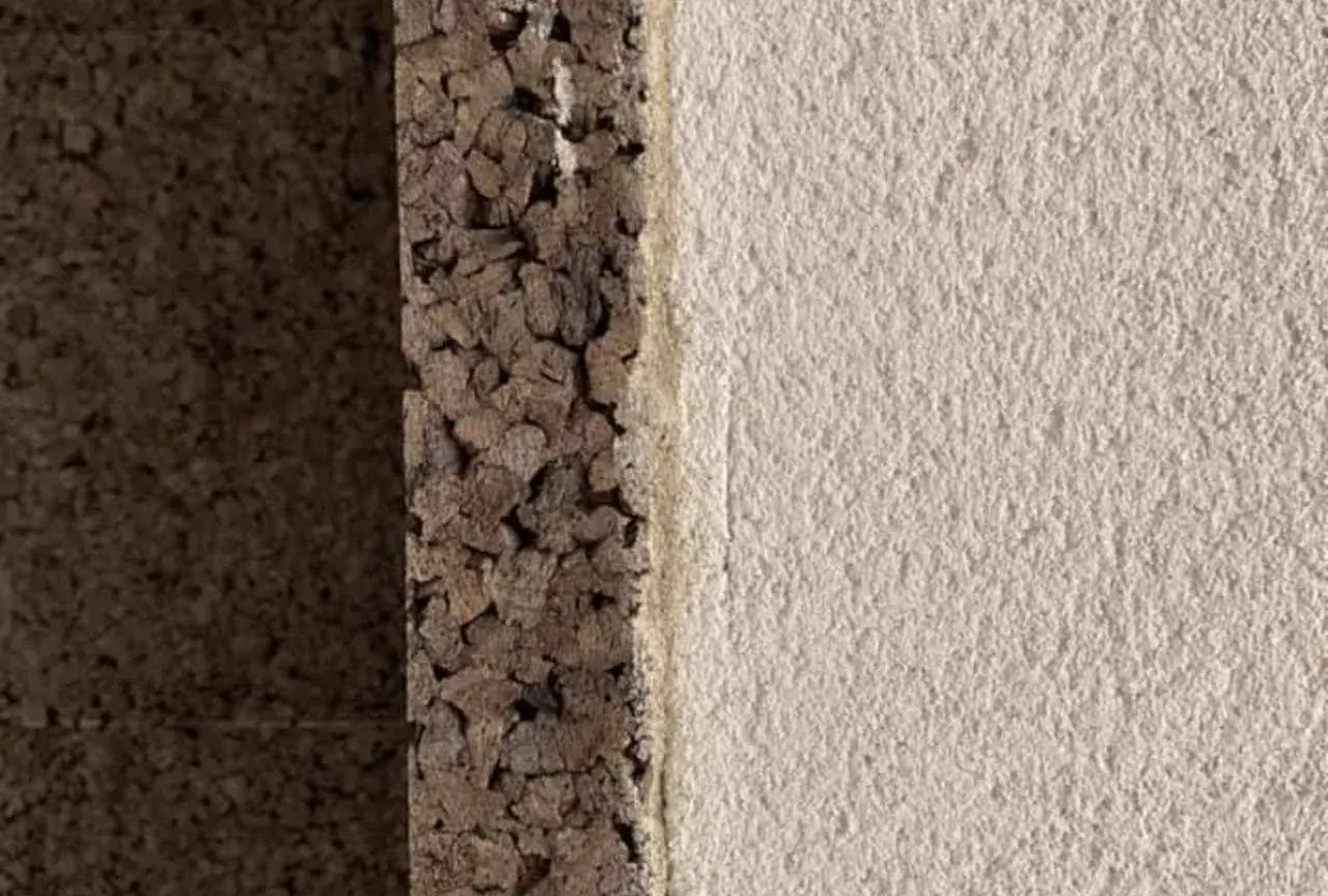 Dettaglio di un muro con strato di intonaco con sughero grezzo e finitura chiara e ruvida.