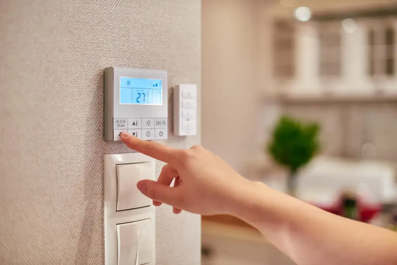 Dito si vede la differenza tra termostato e cronotermostato: un dito preme il pulsante di un termostato digitale impostato a 27 gradi.