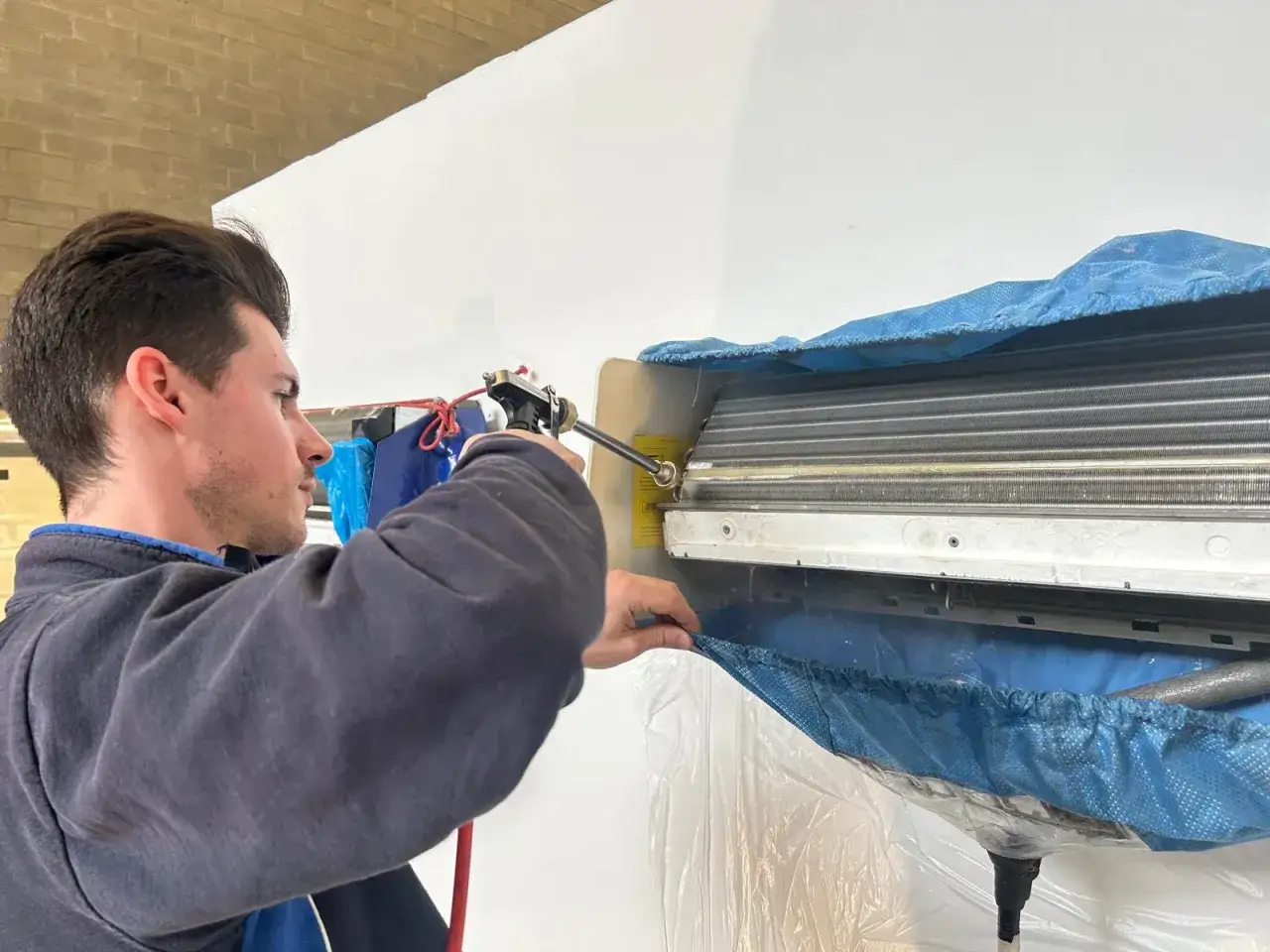 Tecnico che pulisce il condizionatore con uno spray. La procedura per come fare il vuoto al condizionatore è fondamentale per la sua manutenzione.