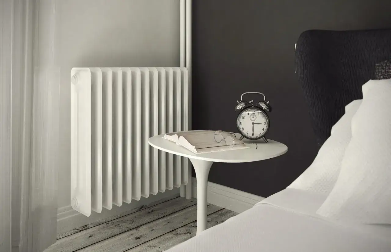 Un classico termosifone sotto una finestra, accanto a un tavolino con libro, occhiali e sveglia.