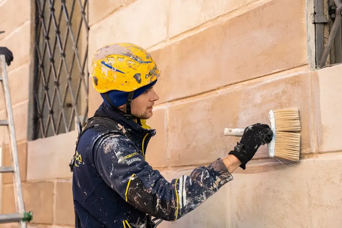 Operaio con casco giallo applica un primo strato di intonaco, il rinzaffo, su una facciata.