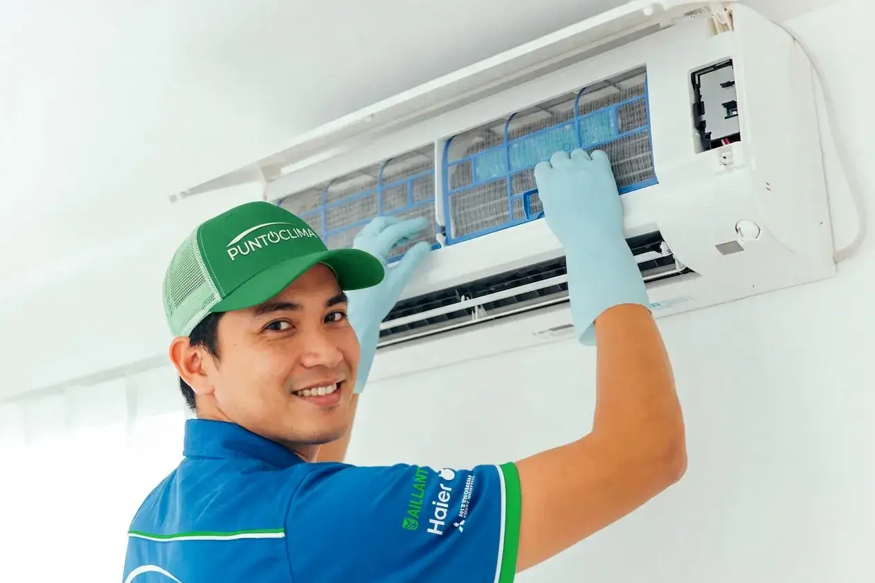 Tecnico sorridente con cappellino e guanti blu esegue la manutenzione condizionatori, pulendo i filtri.