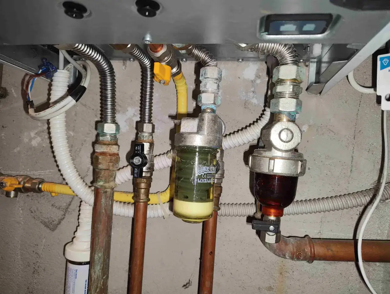 Manutenzione caldaia: pulizia filtro defangatore. Si vedono tubi, valvole e due filtri, uno con liquido giallo e uno con liquido scuro.