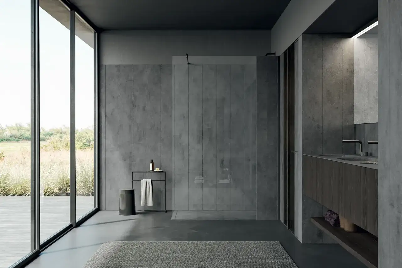 Bagno moderno con pareti in gres effetto cemento e lavabo in materiale Corian. Ampie vetrate affacciano su un giardino rigoglioso.