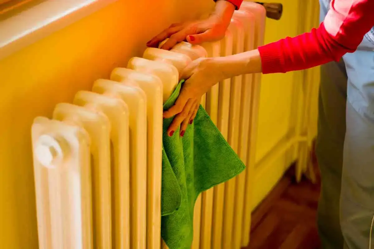 Mani puliscono un termosifone in ghisa con un panno verde. Il lavaggio interno termosifoni in ghisa è importante per l'efficienza.