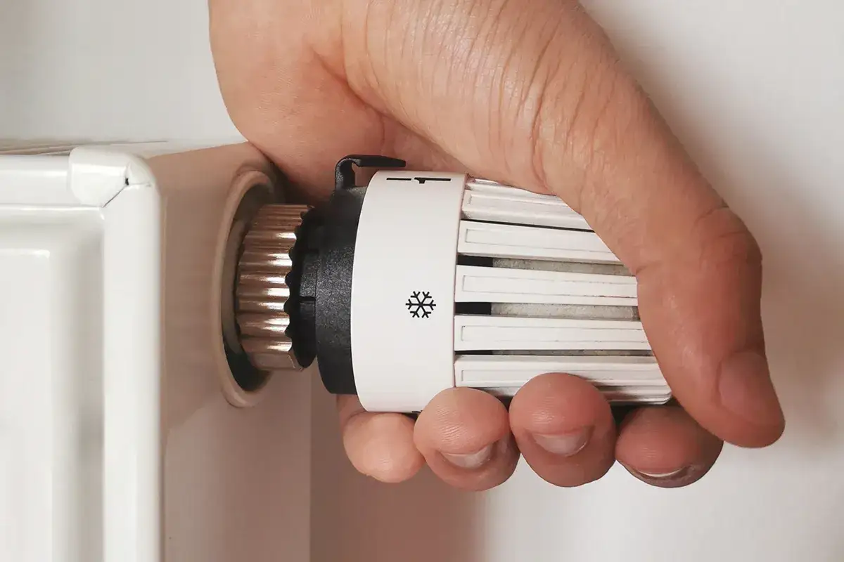 Mano che regola la valvola termostatica di un radiatore, per imparare come regolare valvole termostatiche stanza per stanza.