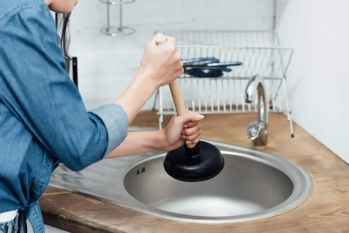 Mani che usano uno sturalavandini per liberare un lavandino intasato. Un rimedio casalingo efficace, come il sale grosso, può aiutare a risolvere il problema.