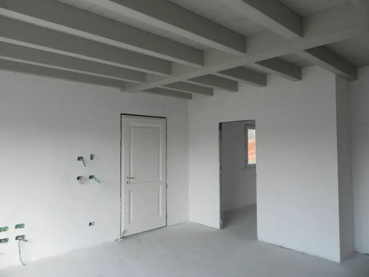 Interno in fase di finitura civile: pareti bianche, soffitto con travi a vista, porte e predisposizioni elettriche.