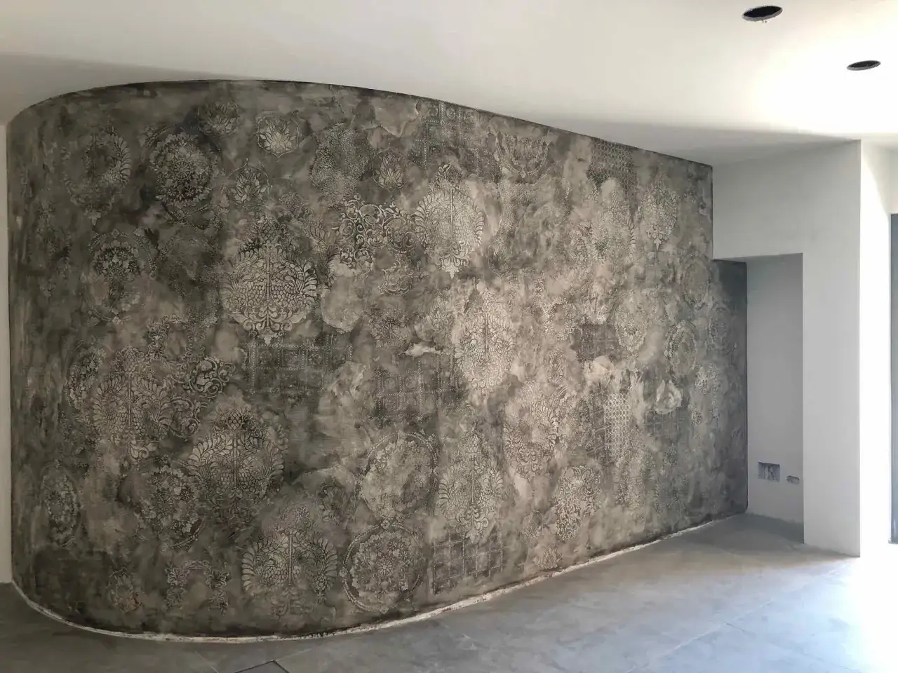 Parete curva con decorazioni floreali e geometriche, effetto materico. Un esempio di come fare intonaco a calce con finitura artistica.