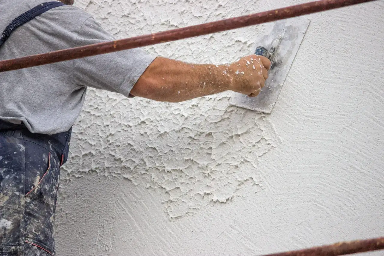 Un operaio applica l'intonaco rustico con una spatola, creando una texture grezza e irregolare su una parete esterna.