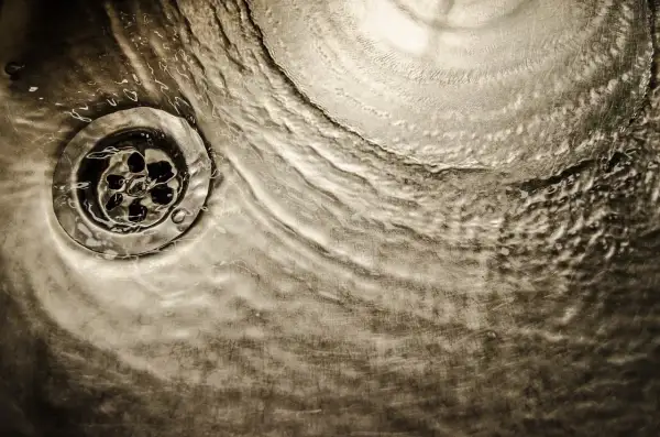 Acqua che scorre su uno scarico metallico, un'immagine che evoca il processo di come sciogliere il grasso nei tubi di scarico.