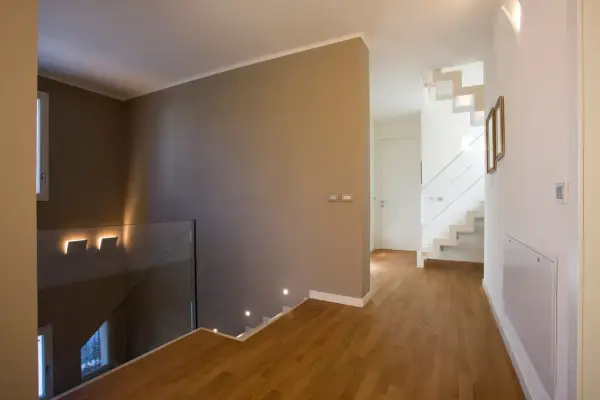 Un moderno disimpegno casa con scala bianca a vista, parapetto in vetro e luci a led che illuminano il corridoio.