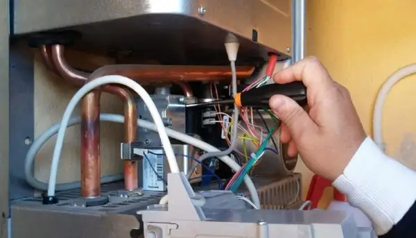 Tecnico effettua la pulizia della caldaia, lavorando sui cablaggi interni con un cacciavite.